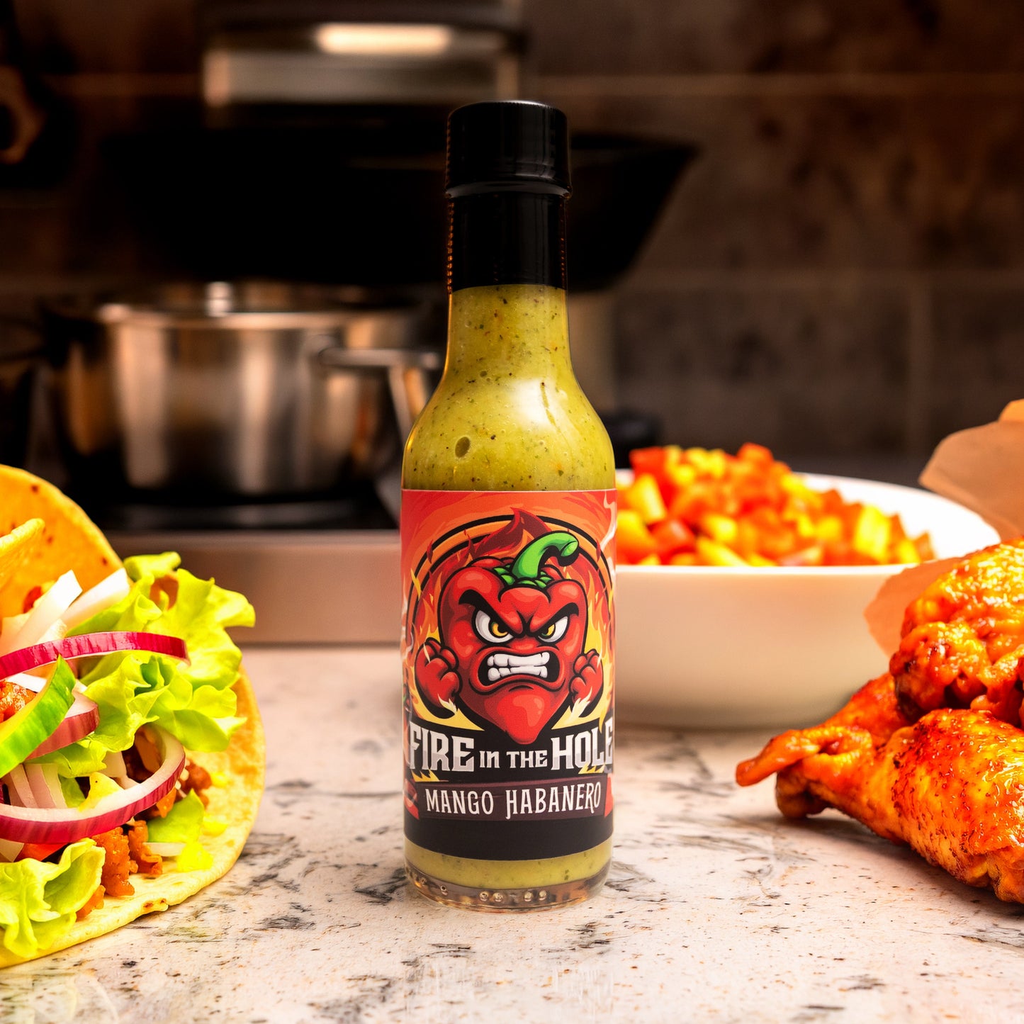 Hot sauce bottle labeled 'Fire in the Hole' with tacos and wings on a counter.